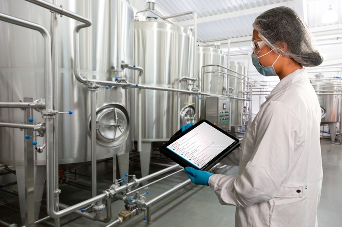 Mulher em pé em uma instalação de produção da indústria alimentícia e verificando o status do Netilion Asset Health