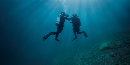 Cena subaquática: um mergulhador ajuda um segundo mergulhador que está tendo problemas com o fornecimento de ar.